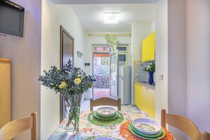 Un'area pranzo con un tavolo apparecchiato per due, un vaso con fiori e vista sulla cucina.