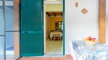 A room with a green shutter door, a dining area with a table and chairs, and a basket of fruit on a table.