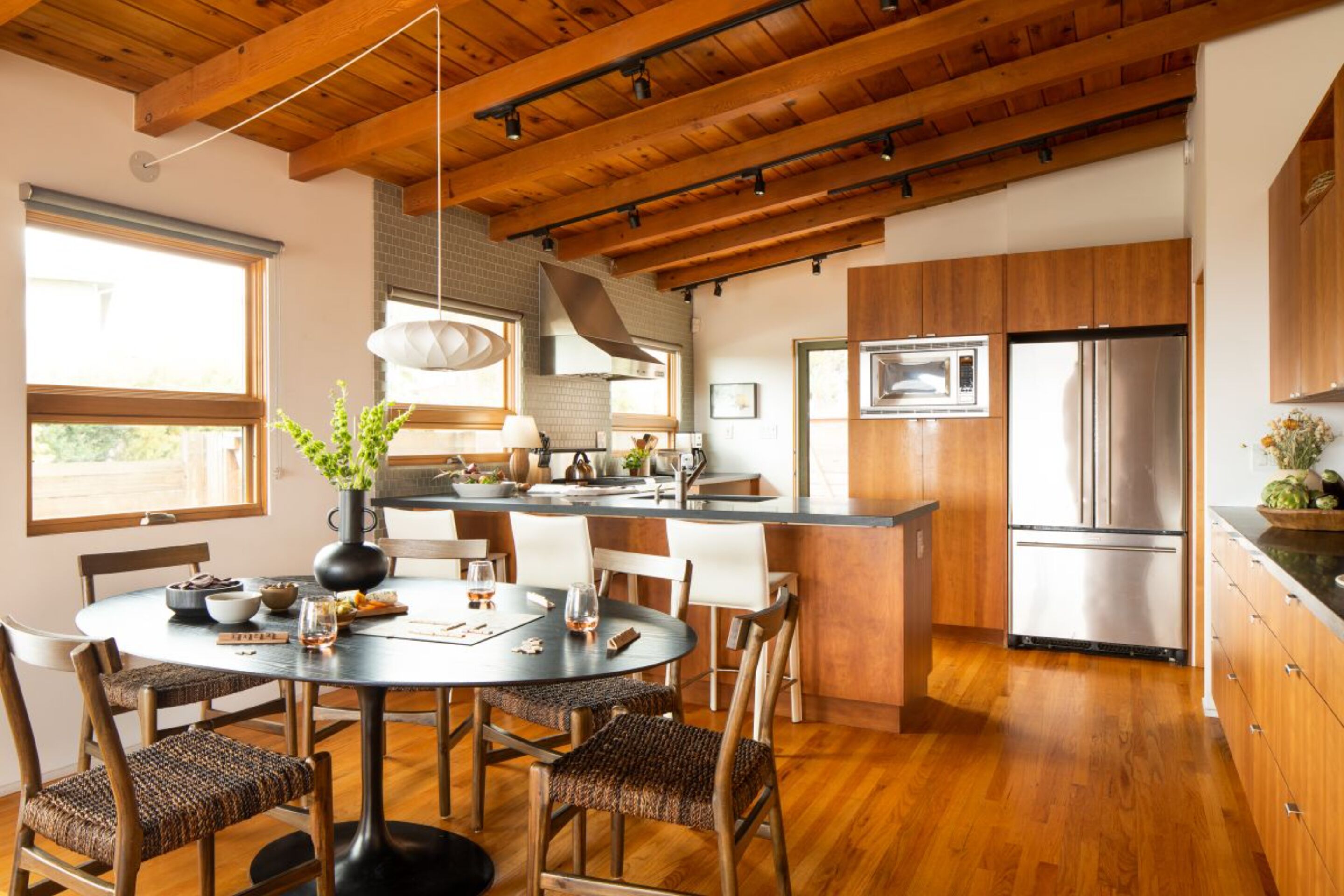 A modern kitchen with wooden cabinets, a stainless steel refrigerator, and a dining area with a round table and chairs.