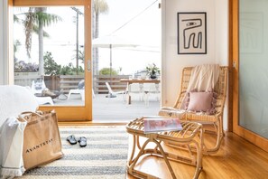 A room with a wicker chair, a wooden table, and a view of the outdoor patio. - Camden by AvantStay | 5mins to the Beach! Elevated Home w/ Pacific Ocean Views (Cardiff By The Sea)