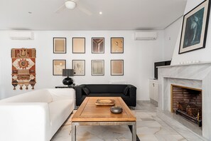 Una sala de estar con chimenea, un sofá negro, una mesa de centro de madera y un sofá blanco.