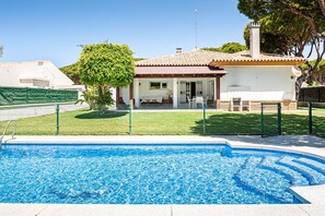 Una piscina con un borde de baldosas, un patio cercado y una casa con techo de tejas y una chimenea.
