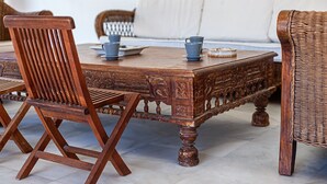 A wooden dining table with chairs, a woven sofa, and a white wall in the background.