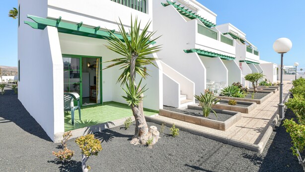 Un edificio moderno con fachada blanca, detalles en verde y un jardín bien cuidado.