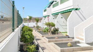 Un patio con un edificio blanco, barandillas verdes y un jardín de cactus.
