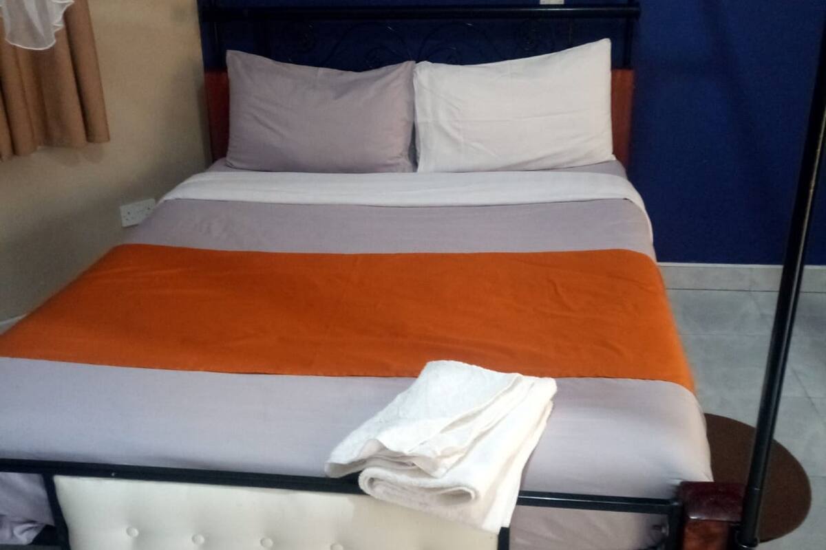 A bed with a white headboard, grey and orange bedding, and a folded white towel.