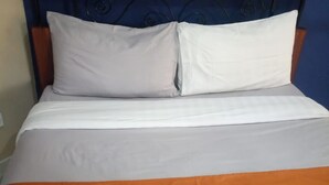 Una cama con colcha blanca y naranja, cabecera de madera y pared azul.