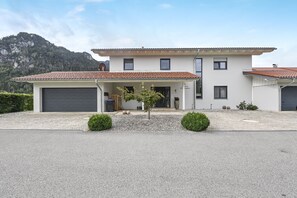 Une maison à deux étages avec un garage, un petit arbre dans l’allée et une montagne en arrière-plan.