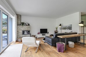 Un salon moderne avec une cheminée en pierre, un téléviseur à écran plat, un canapé, une table à manger et une grande fenêtre.