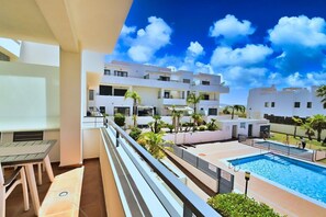 A residential building with a pool, outdoor furniture, and a clear blue sky.