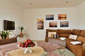 A living room with a brown sofa, a glass coffee table with strawberries, a TV, and wall art.