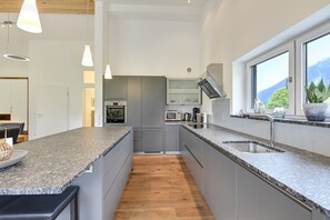 Une cuisine moderne dotée de plans de travail en granit, d’un four encastré et d’une grande fenêtre offrant une vue sur les montagnes.