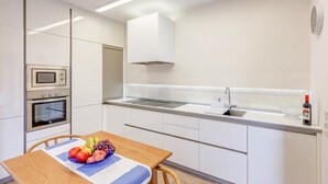Une cuisine moderne avec des meubles blancs, un four encastré, un four à micro-ondes et un évier en acier inoxydable.