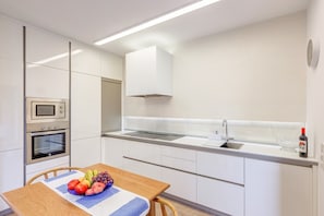 Une cuisine moderne avec des meubles blancs, un four encastré, un four à micro-ondes et un évier en acier inoxydable.