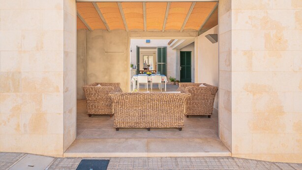 Un espace extérieur aménagé avec des meubles en osier, une table et des chaises, le tout délimité par un mur en pierre.