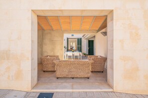 An outdoor seating area with wicker furniture, a table, and chairs, enclosed by a stone wall.