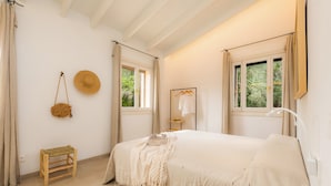 Quarto com cama, cesto pendurado, um banquinho pequeno e um espelho na parede.