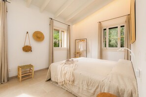 Une chambre à coucher avec un lit, une corbeille suspendue, un petit tabouret et un miroir au mur.