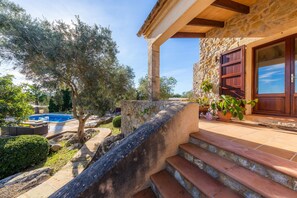 A stone house with a pool, steps leading to a wooden door, and surrounding greenery. - Romantic Natural Stone Finca with Pool, Garden, Rooftop Terrace and Wi-Fi (Artá)