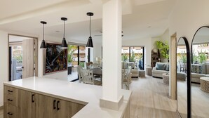 A modern kitchen with a large island, pendant lighting, and a dining area with a view of the outdoors.
