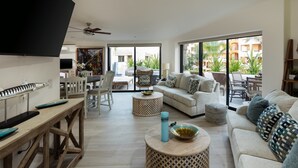 A spacious living room with a large TV, a wooden dining table, and a sofa with patterned cushions.