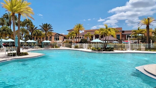 Una piscina con una cerca blanca, palmeras y edificios al fondo.