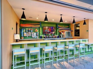 A bar area with a counter, multiple hanging lights, a television screen, and several chairs.