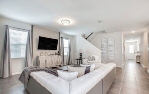A modern living room with a sofa, a flat-screen TV, and a staircase leading to another level.