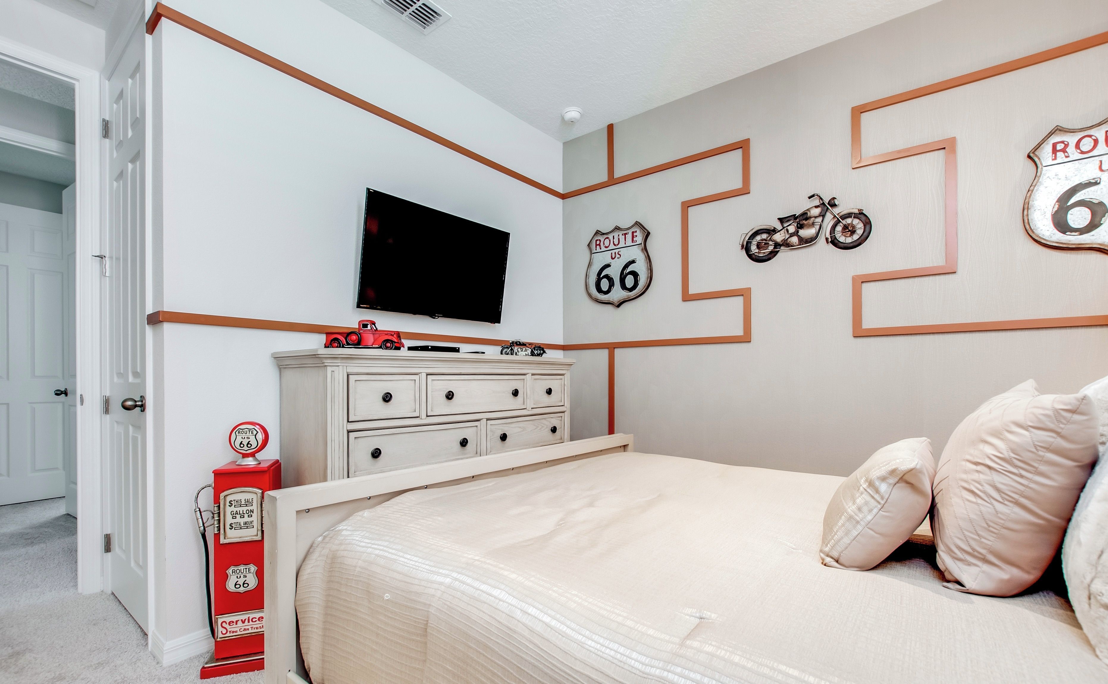 A bedroom with a bed, dresser, and wall decorations including Route 66 signs and a motorcycle.