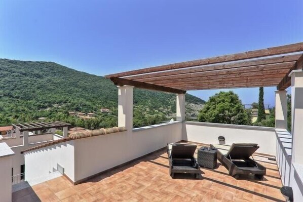Una terrazza sul tetto con due poltrone, un pergolato e vista su un pendio verde.