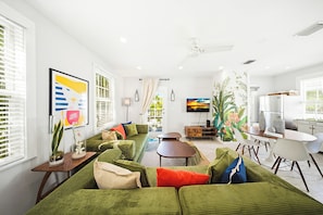 A modern living room with a green sofa, a dining table, and a kitchen area.