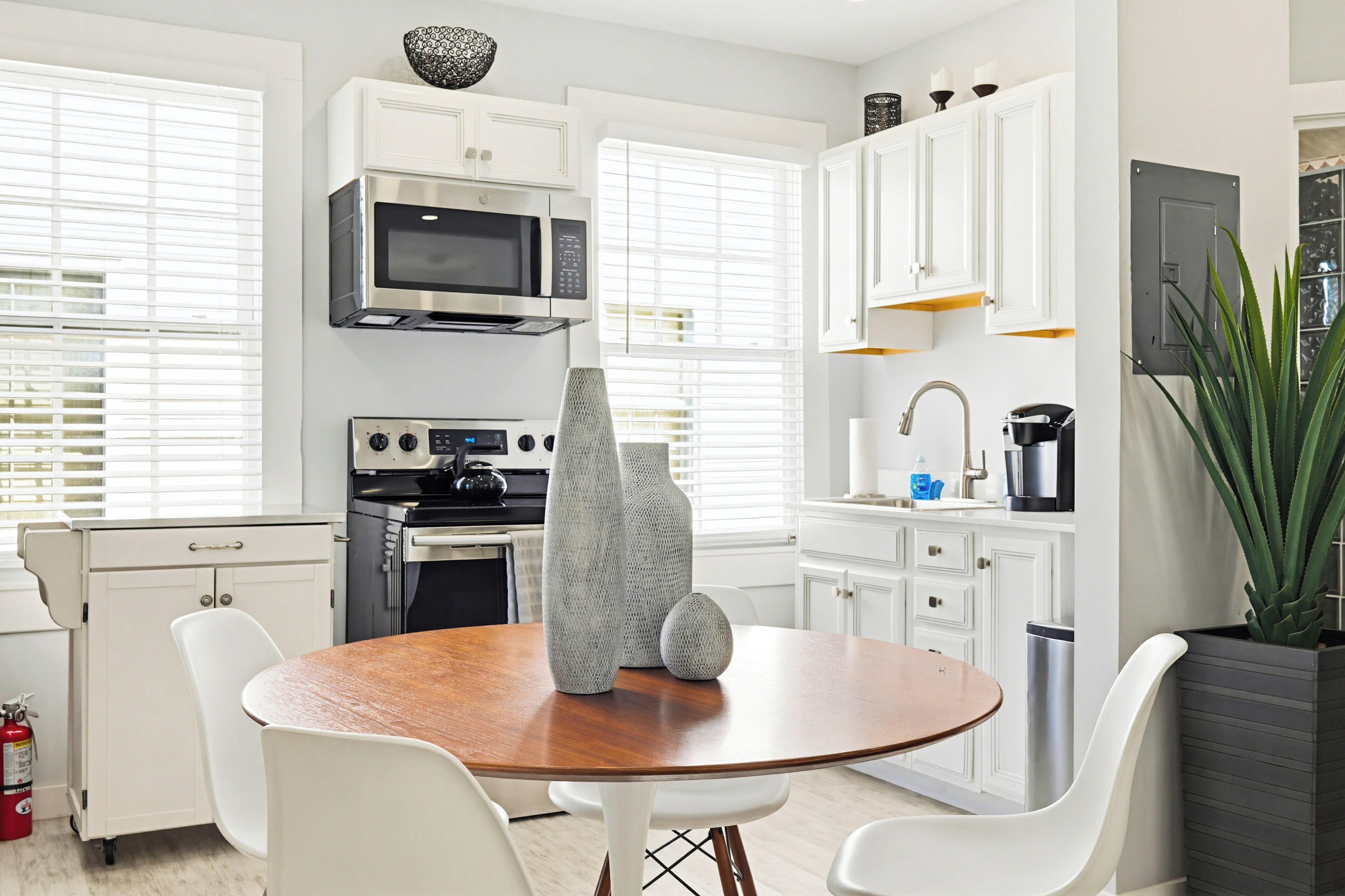 Een moderne keuken met witte kastjes, een magnetron, een oven, en een eethoek met een houten tafel en witte stoelen.