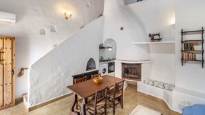 A dining area with a wooden table and chairs, a white wall with a built-in washing machine, a fireplace, and a bookshelf. - The flair of Ibiza on the coast — Casa Morrás 41 (Felanitx)