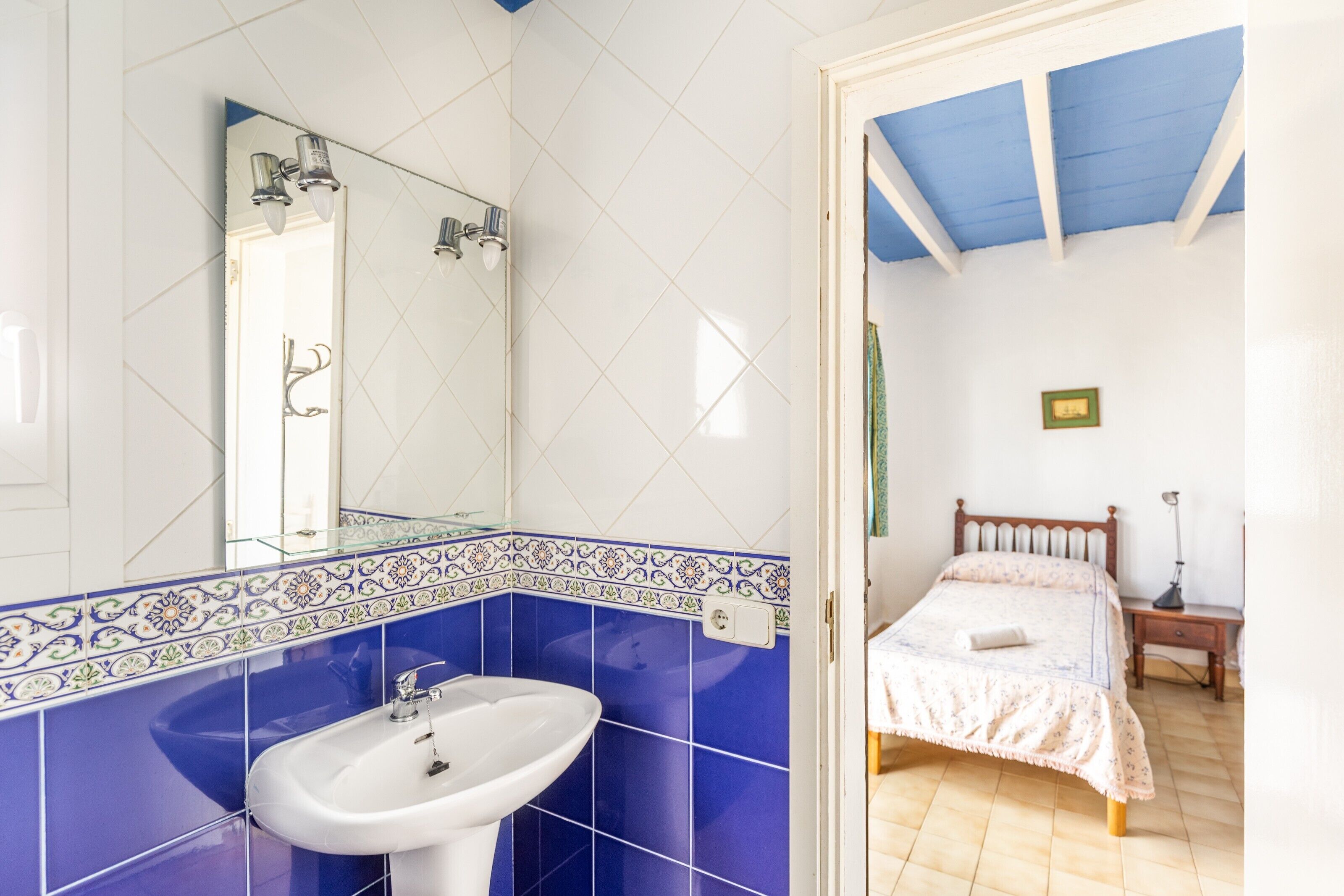 Een badkamer met een wit wastafelmeubel, blauwe tegels en een spiegel.