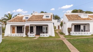 A row of white buildings with tiled roofs, a paved walkway, and a grassy area. - The flair of Ibiza on the coast — Casa Morrás 41 (Felanitx)