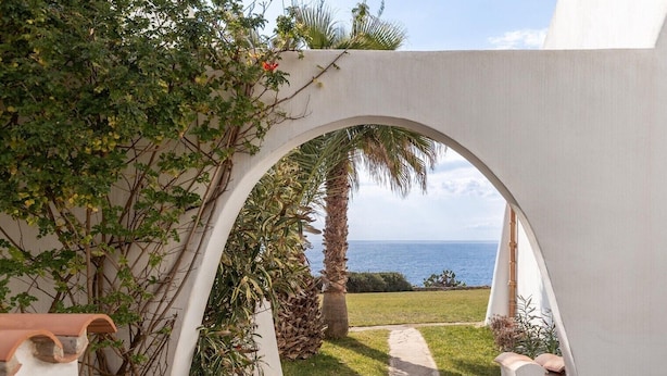 A white arched pathway leading to a view of the sea, surrounded by greenery and a palm tree. - The flair of Ibiza on the coast — Casa Morrás 41 (Felanitx)