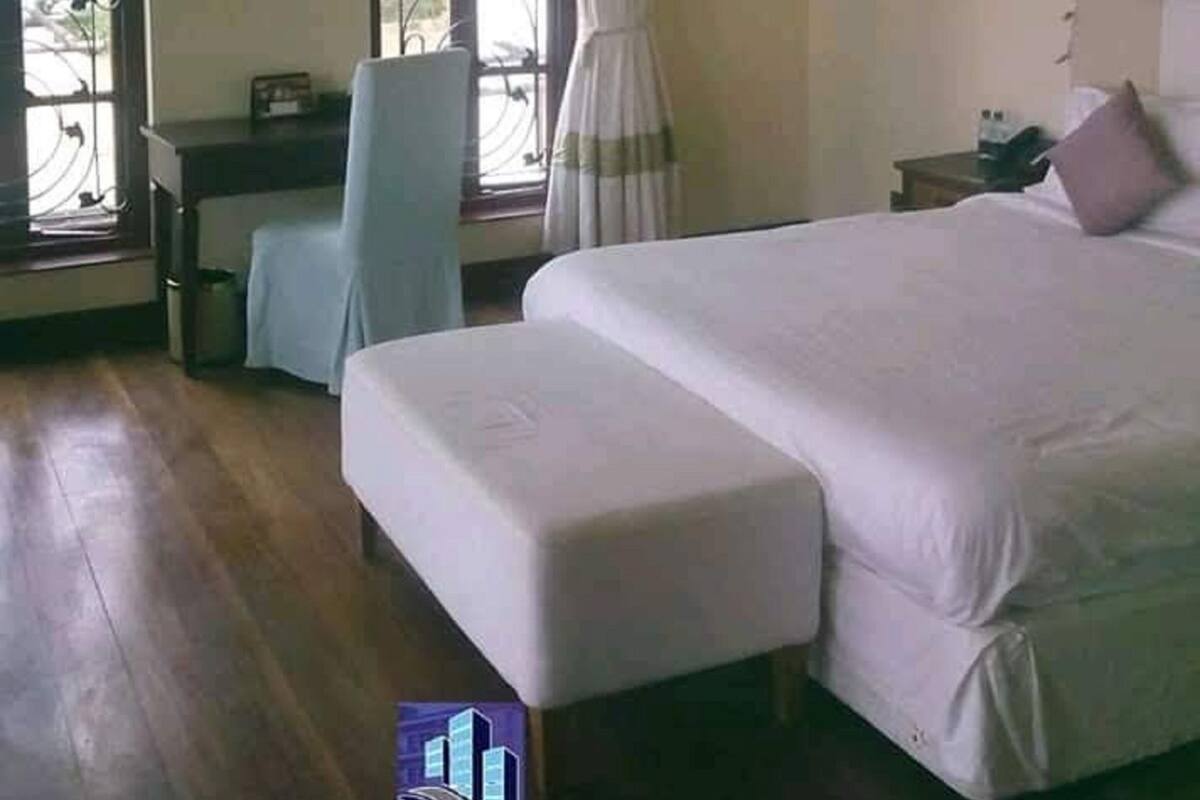 A bedroom with a bed, a desk, and a chair. There are windows with curtains.
