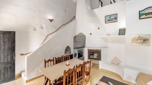 Un espace repas avec une table et des chaises en bois, un escalier, une cuisine et un coin salon avec un canapé et des coussins.