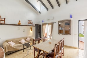 A spacious room with a wooden dining table, a sofa, and a window with curtains.