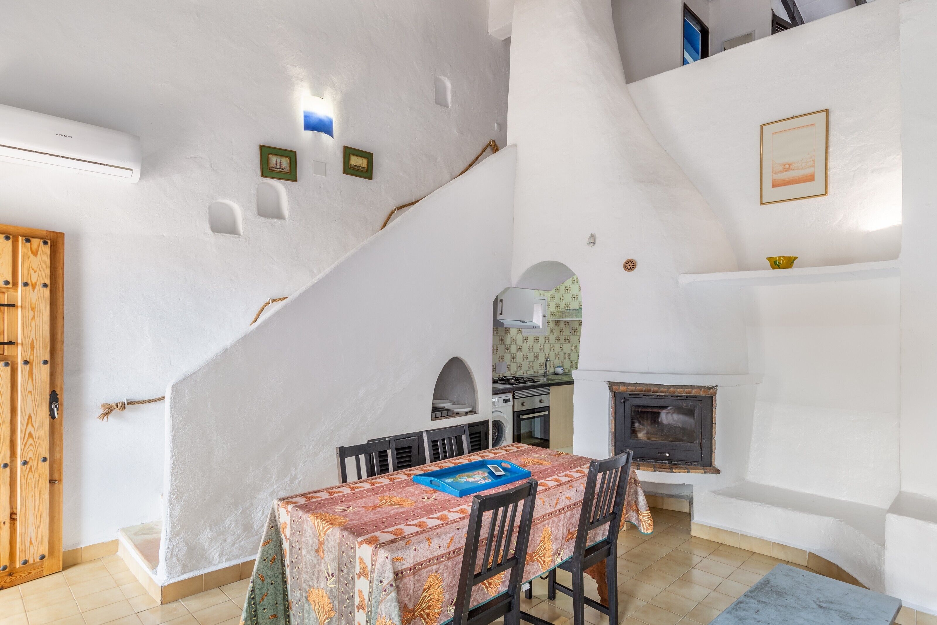 Un comedor con una mesa dispuesta para cuatro personas, una chimenea y una cocina al fondo.