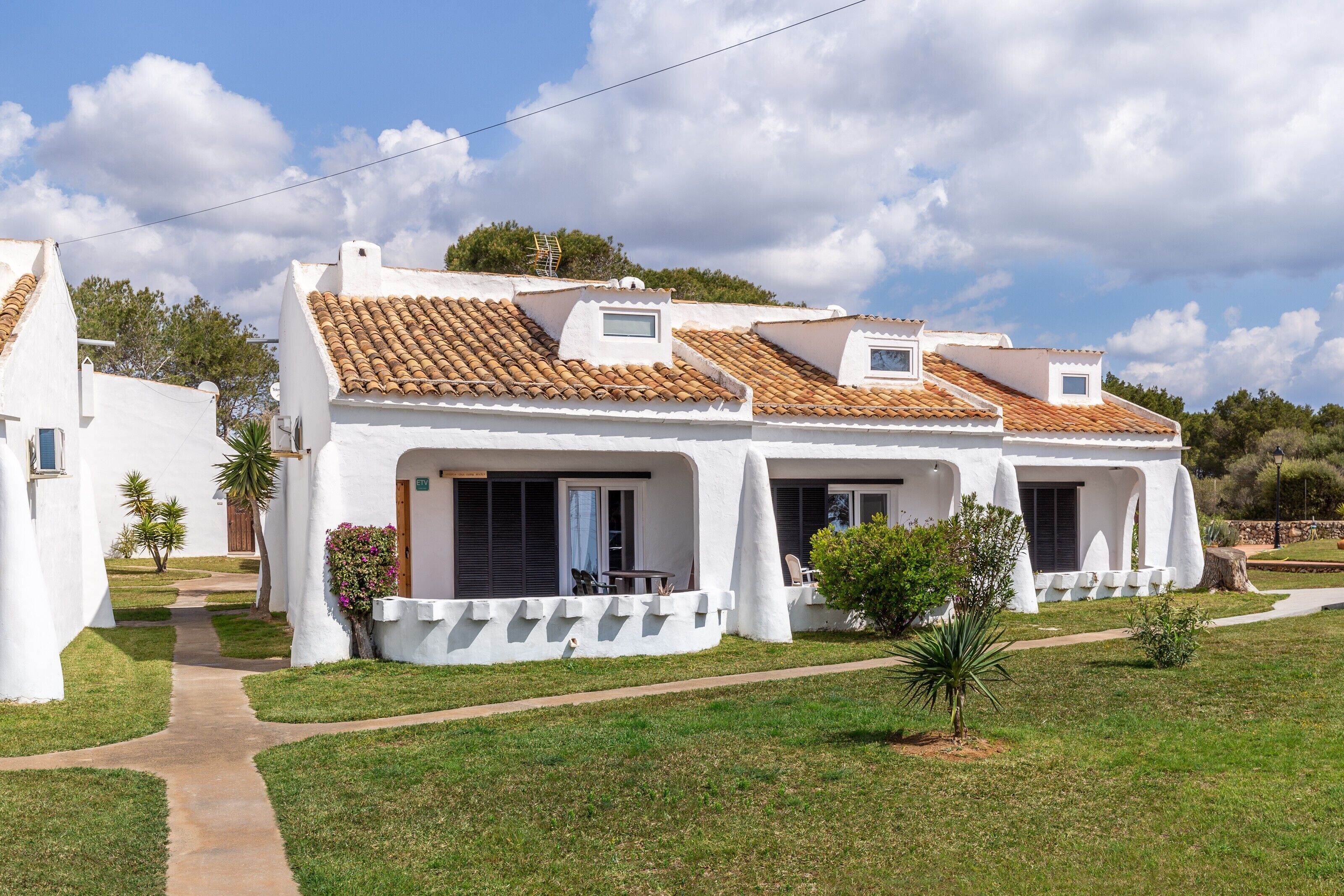 A white villa with a tiled roof, a paved driveway, and a small garden.
