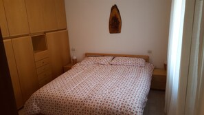 A bedroom with a bed, wooden wardrobe, and a wall-mounted decoration.