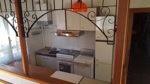 Une cuisine compacte équipée d’une cuisinière, d’un évier et d’un four, d’un petit égouttoir et d’une fenêtre ornée de barreaux en métal décoratifs.
