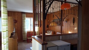 L’intérieur d’un chalet en bois, avec un lit, une petite table, une chaise rouge et une fenêtre avec des rideaux.
