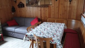 A wooden interior with a sofa, a table with a floral tablecloth, and a bench.