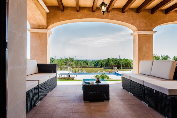 A covered outdoor seating area with a view of a swimming pool and landscape.