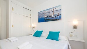 A hotel room with a bed, two pillows, a painting of boats, and a nightstand with a lamp.