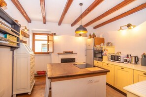 A compact kitchen with wooden beams, a central island, a refrigerator, a microwave, and a sink.