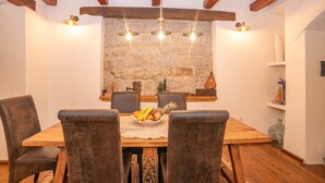 Un comedor con una mesa de madera, cuatro sillas, un frutero y una pared de piedra con una lámpara colgante.