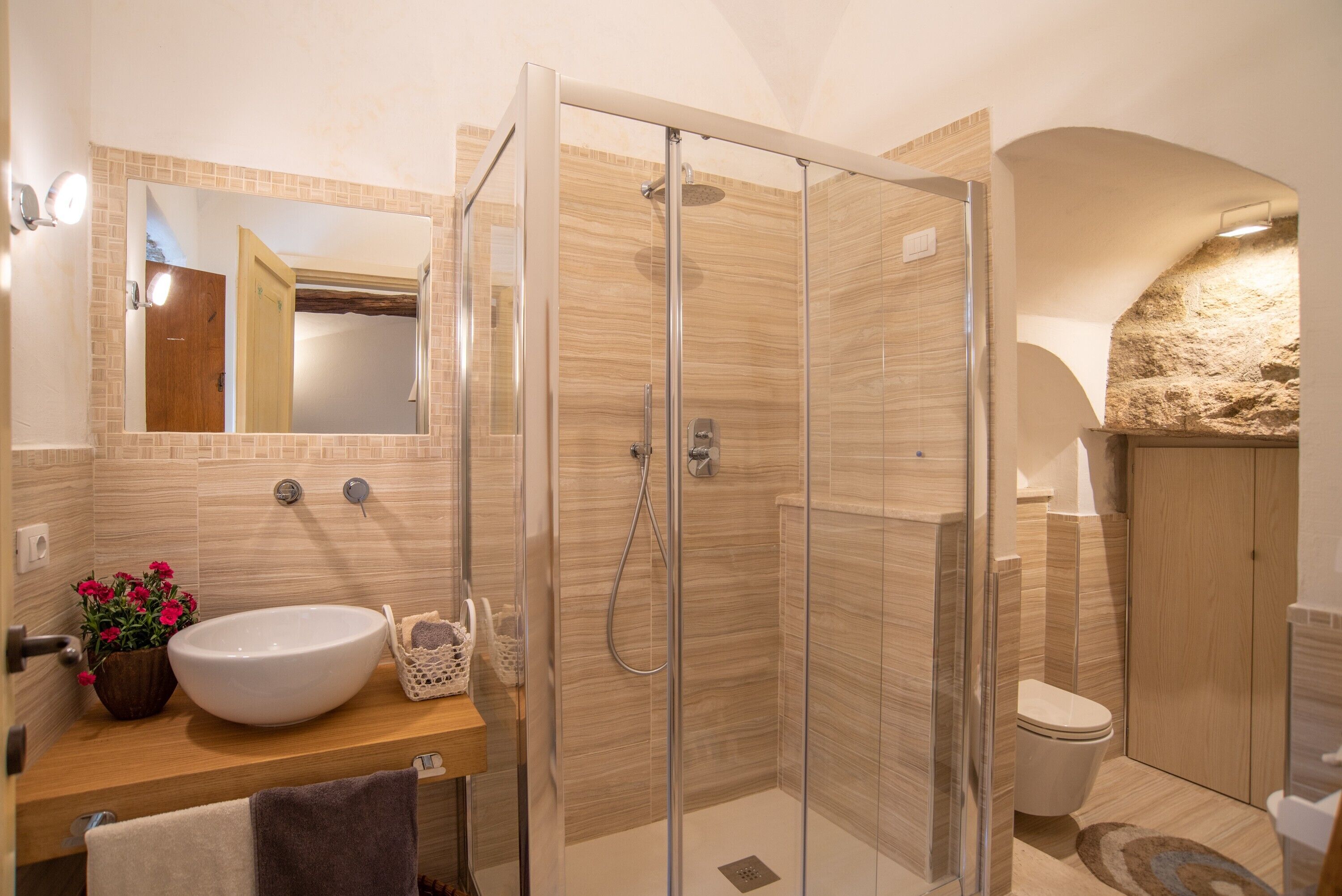 A bathroom with a glass-enclosed shower, a sink with a vase of flowers, and a mirror above the sink.